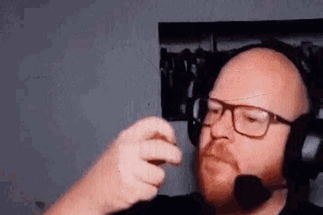 a bald man with a beard wearing headphones and a microphone is talking on a video call .