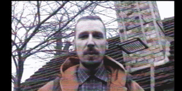 a man in a plaid shirt and vest is standing in front of a building