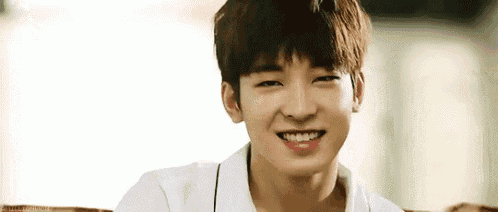 a young man is smiling while sitting on a couch and wearing a white shirt .