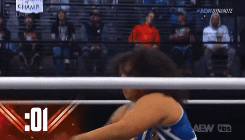 a woman in a blue and white tank top is wrestling in a ring with a crowd watching .