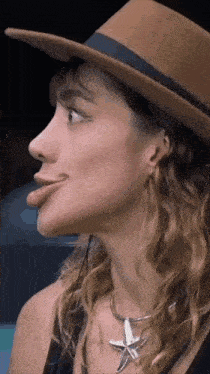 a woman wearing a hat and a necklace with a starfish pendant is sticking her tongue out .
