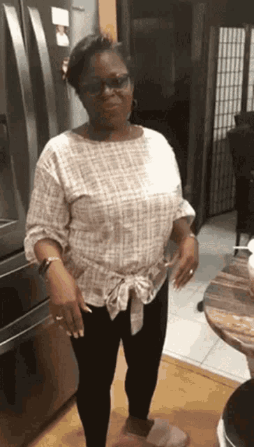a woman wearing glasses and a white shirt is standing in front of a refrigerator .