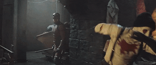 a man in a red suit is holding a sword and standing next to another man in a white jacket .