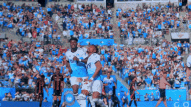 two soccer players are celebrating a goal in front of a crowd wearing jerseys that say fly