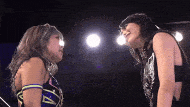 two women are standing next to each other in a wrestling ring and looking at each other .