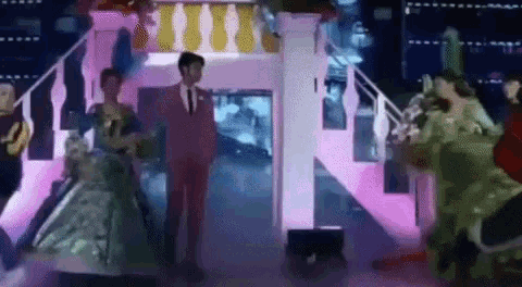 a man in a pink suit and tie is standing next to a woman in a blue dress on a stage .