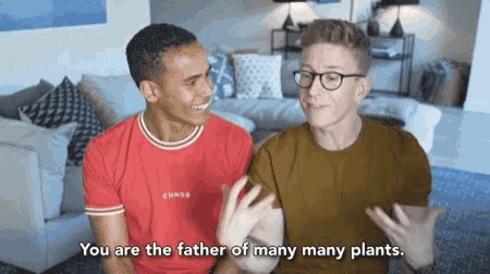 two men are sitting on a couch and one of them is saying " you are the father of many many plants "