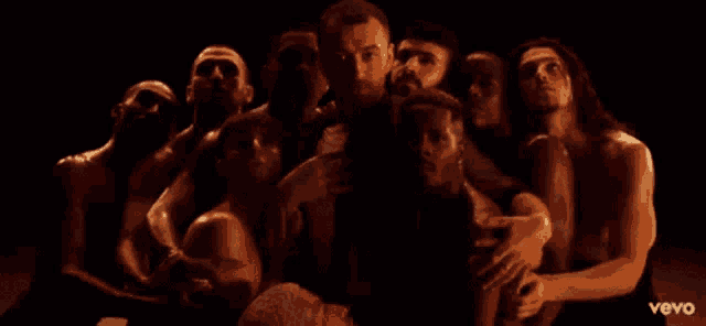 a man is surrounded by a group of naked people with the word vevo on the bottom right