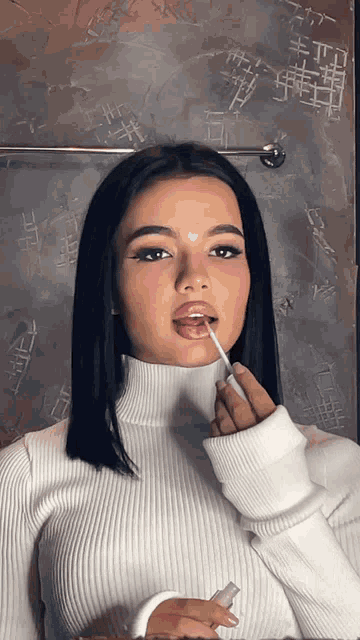 a woman in a white sweater is applying lip gloss to her lips