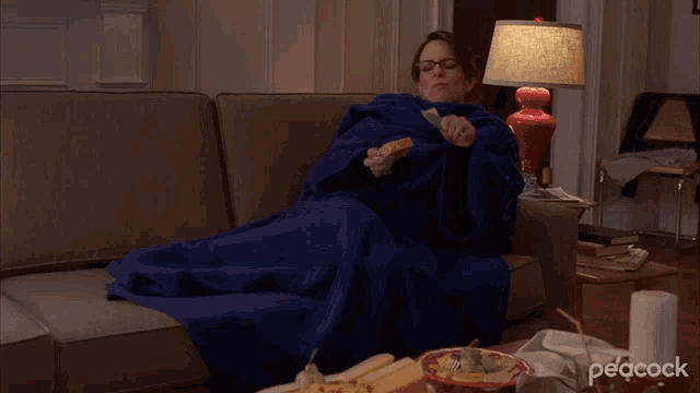 a woman wrapped in a blue blanket sits on a couch with peacock written on the bottom