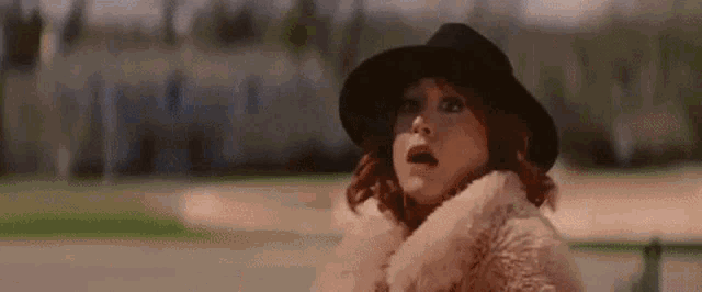 a woman wearing a hat and a fur coat is looking at the camera .