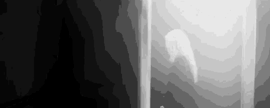 a black and white photo of a person standing in a foggy room in a dark room .