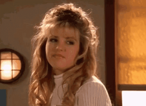 a woman with long blonde hair is wearing a white sweater and making a funny face .