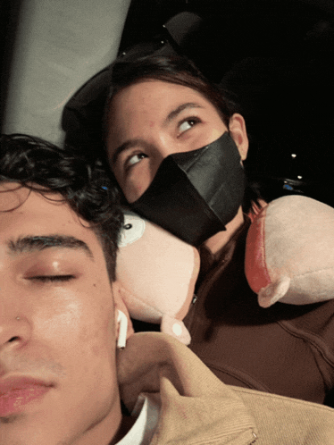 a woman wearing a black mask is holding a stuffed animal next to a man