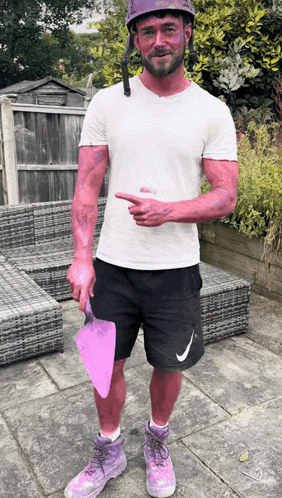 a man with purple paint on his face and arms holds a pink spatula