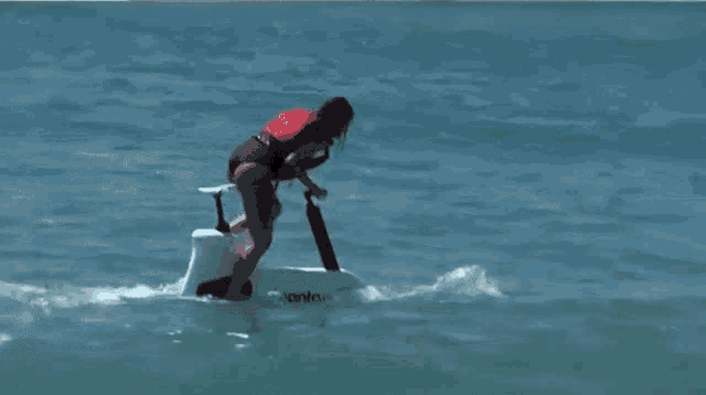 a woman in a red vest is riding a surfboard in the ocean