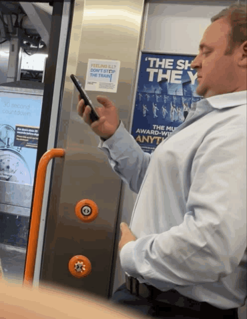 a man sitting on a train looking at his phone with a poster on the wall that says the sh they