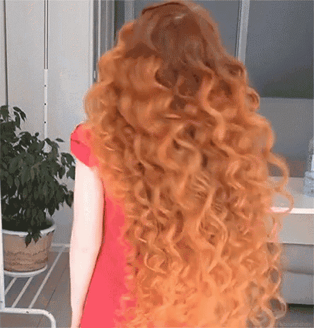 a woman with long red curly hair is wearing a red dress .