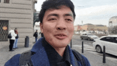 a man wearing a blue coat and a black shirt is standing in front of a white car .
