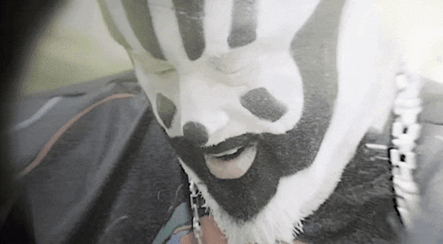 a man with black and white face paint and a beard is wearing a mask .