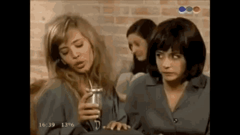 a group of women are sitting next to each other in a room . one of the women is holding a can of soda .