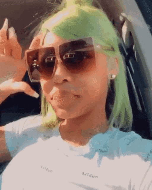 a woman with green hair is wearing sunglasses and making a funny face .