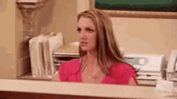 a woman in a pink shirt is sitting at a counter looking at something .