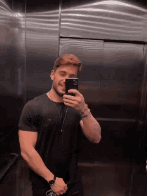 a man in a black shirt is taking a selfie in an elevator .