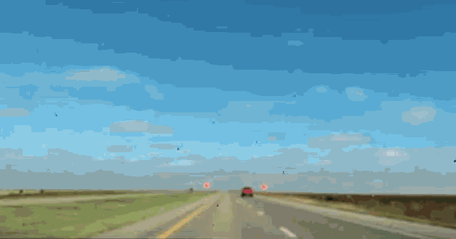 a red truck is driving down a highway with a blue sky in the background