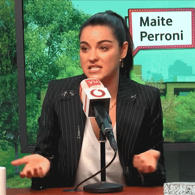 a woman talking into a microphone with a sign that says maite perroni in the background