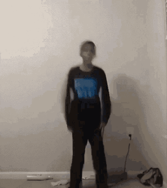 a blurry picture of a person standing in a room wearing a blue shirt .