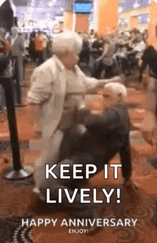 an elderly couple is dancing in a crowded room and the woman is holding the man 's leg .