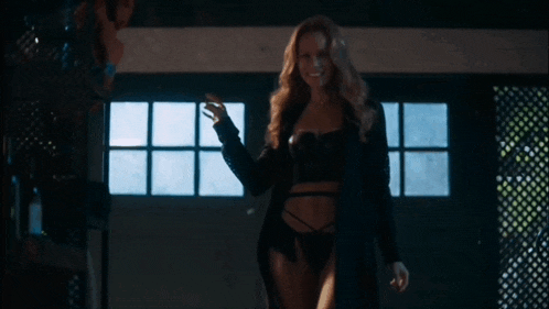 a woman in lingerie and a black coat is standing in front of a window .