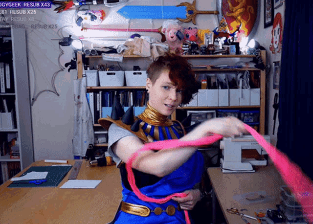 a woman in a blue and gold costume is holding a pink ribbon in front of a shelf that says resub