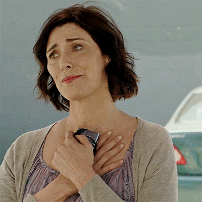 a woman wearing a cardigan and a purple dress is smiling and holding a cell phone