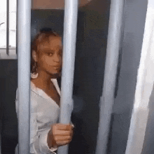 a woman is behind bars in a jail cell holding onto a metal bar .