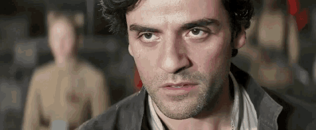 a close up of a man 's face with a beard and a woman in the background .