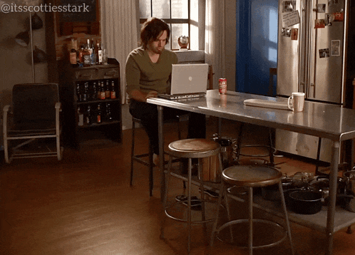 a man sits at a table using a laptop with the hashtag itsscottiesstark at the bottom
