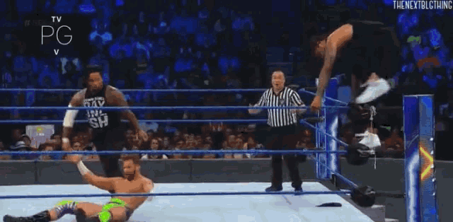 a wrestler is jumping in the air during a match while a referee watches .