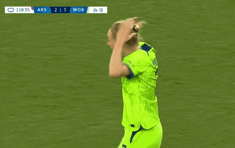 two female soccer players hugging each other on a field with a scoreboard in the background