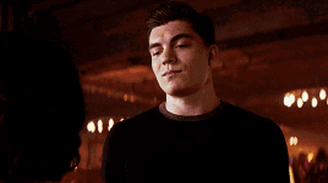 a man in a black sweater stands in front of a woman in a dark room