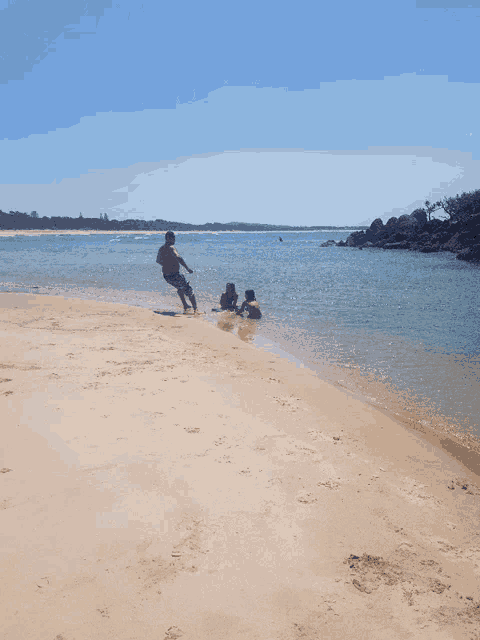 a man and two children are playing on a beach near the water