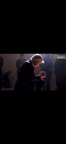a man in a suit and tie is kneeling down and praying in front of a crowd of people