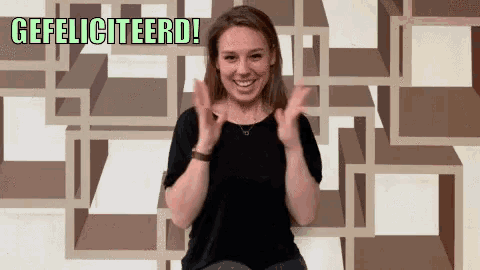 a woman applauds in front of a wall with the words gefeliciteerd above her