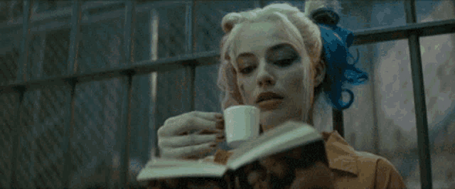 harley quinn is reading a book and drinking from a cup .