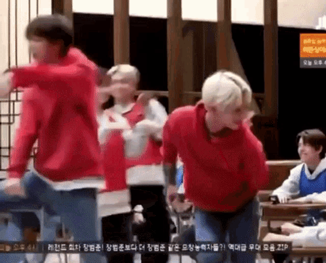 a group of young men are dancing in a room while wearing red sweatshirts .