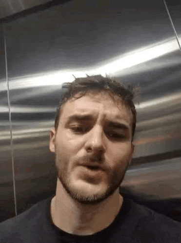 a man with a beard is standing in an elevator and making a face .