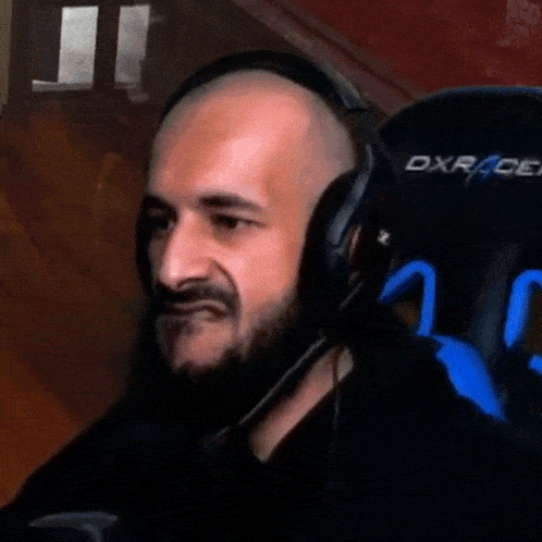 a bald man with a beard is wearing headphones and sitting in a dxrace chair .