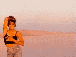 a woman in a crop top and jeans is standing in the desert .