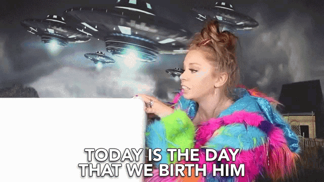 a woman in a colorful fur coat is pointing at a white board with the words today is the day that we birth him